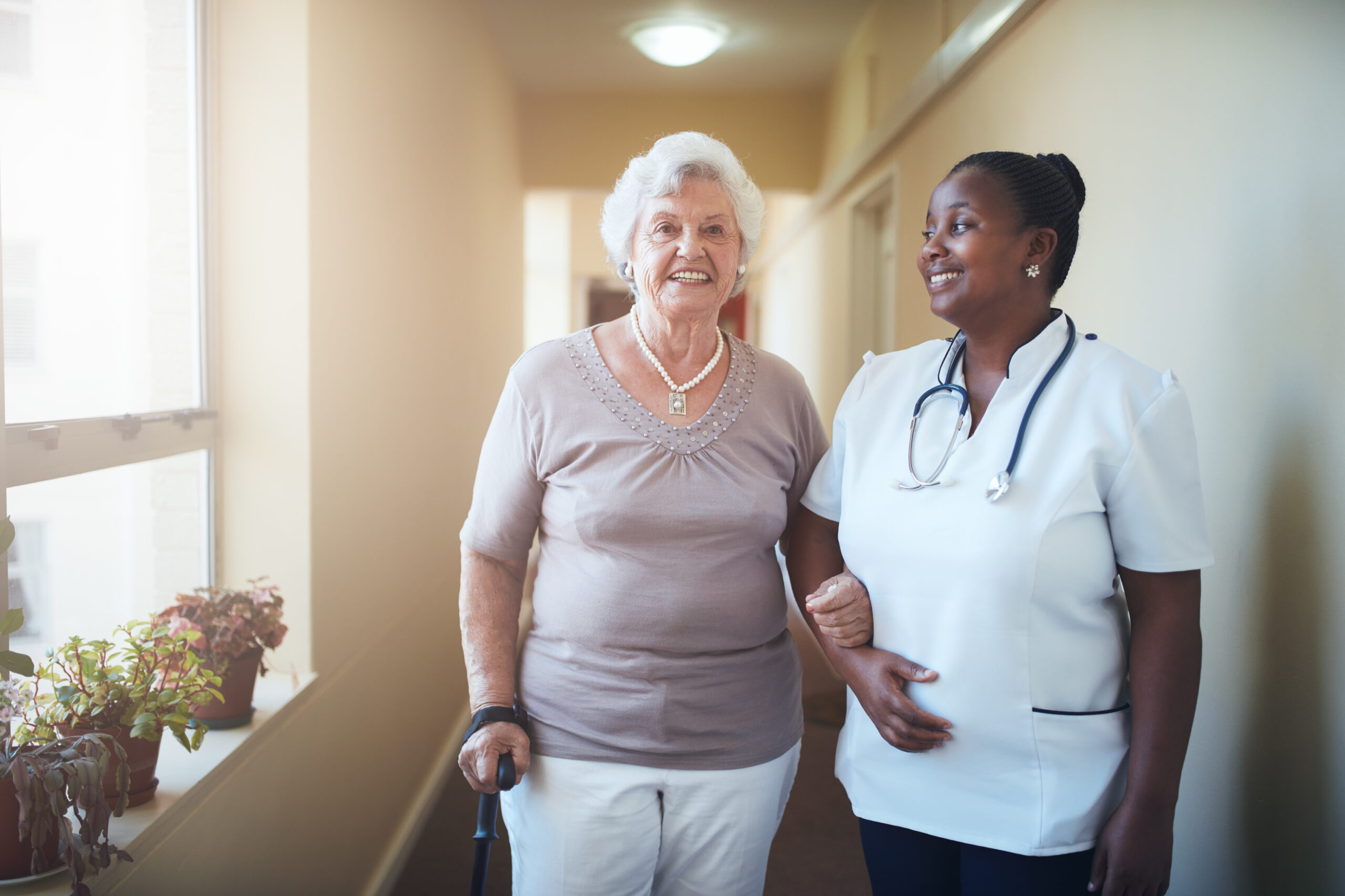 Happy healthcare worker and senior woman together at nursing home. Caring female doctor assisting a senior patient to walk.
